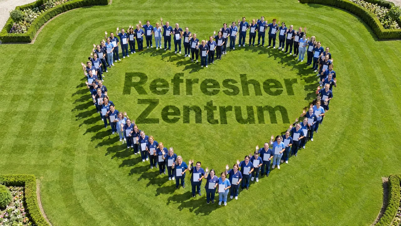 Viele Fachkräfte in blauer Kleidung bilden auf einem Rasen ein großes Herz, in der Mitte steht Refresher Zentrum im Gras.